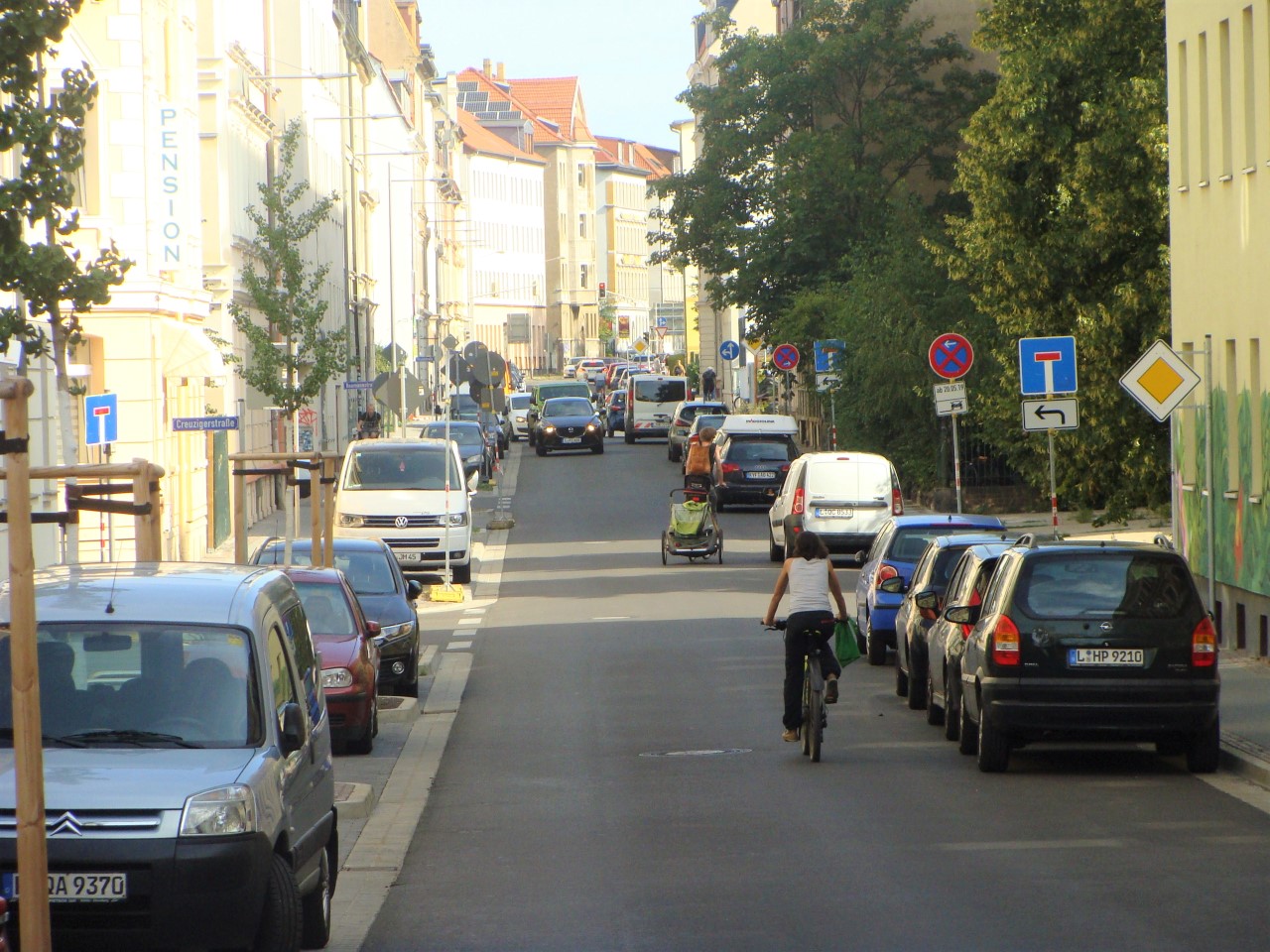 Zoom in die sanierte Gießerstraße mit geparkten Autos links und rachts am Straßenrand, sowie RadfahrerInnen und Autos auf der Fahrbahn