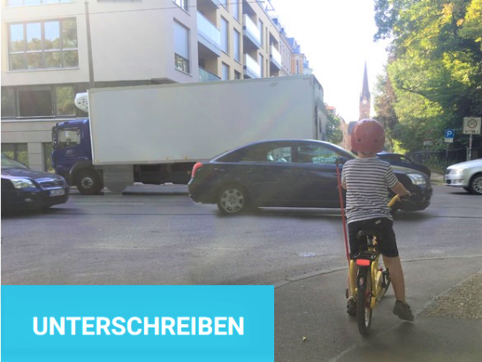 Kind auf Fahrrad steht vor der Käthe-Kollwitz-Straße mit seinem Fahrrad. Wegen des starken Verkehrsstroms aus Autos und LKW kommt es nicht über die Straße